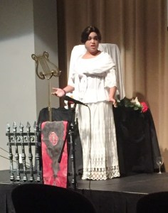 The Ghoulish Wife stands and sings before the prized Poe Toaster scarf